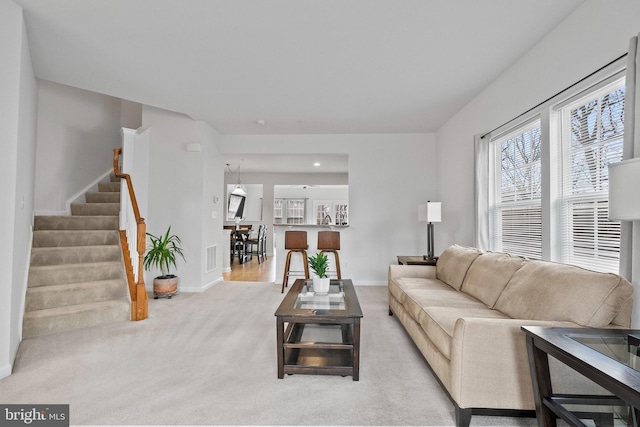 carpeted living area featuring baseboards, visible vents, and stairway