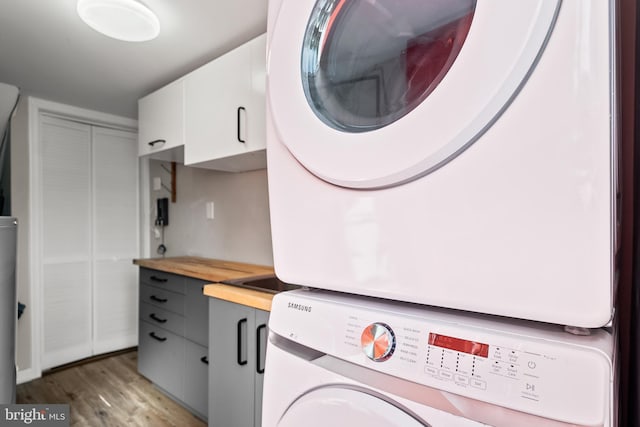 clothes washing area with stacked washer and clothes dryer, light wood-style flooring, and cabinet space