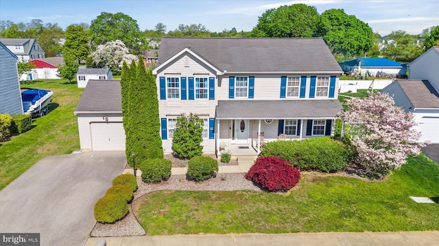 colonial-style house featuring covered porch, driveway, a front lawn, and a garage