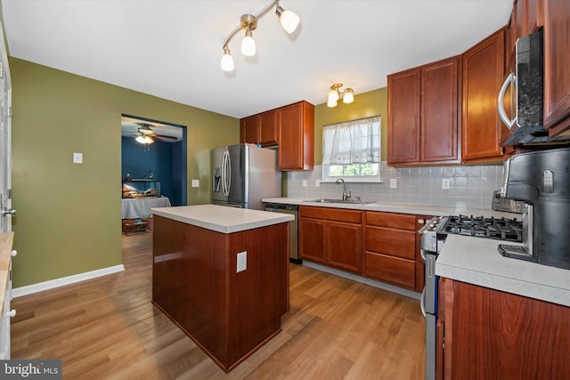 kitchen with appliances with stainless steel finishes, a sink, light wood-style floors, light countertops, and decorative backsplash