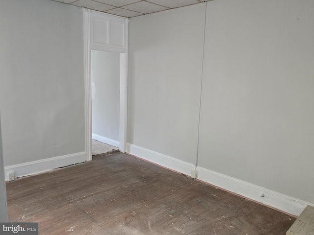 empty room with baseboards, a drop ceiling, and wood finished floors