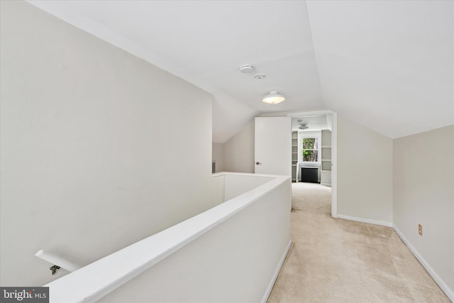 hallway featuring baseboards, an upstairs landing, vaulted ceiling, and light carpet