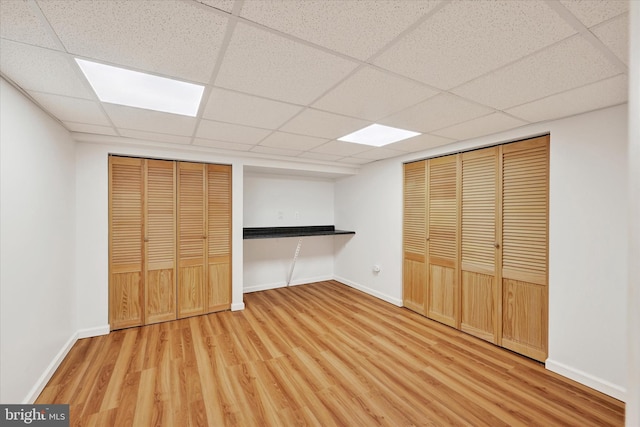 unfurnished bedroom with baseboards, a drop ceiling, and wood finished floors