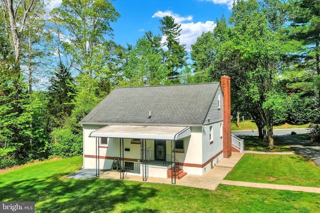 back of property with a yard, a chimney, and roof with shingles