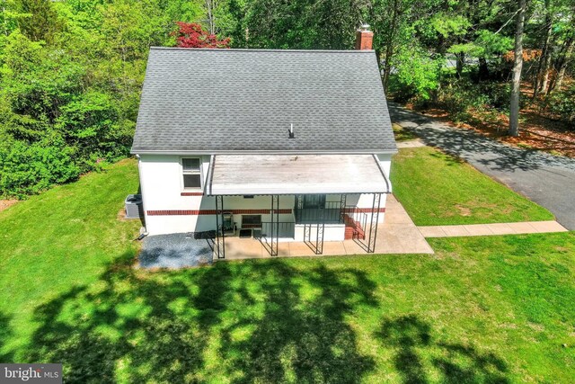 rear view of property with a lawn, roof with shingles, a chimney, and a patio