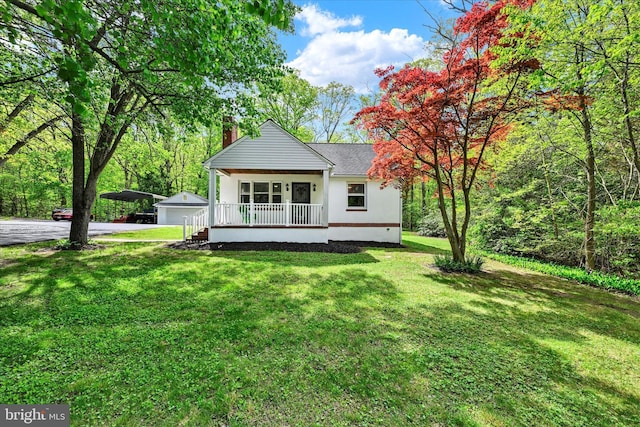 back of house featuring an outdoor structure, covered porch, a chimney, a yard, and a detached garage