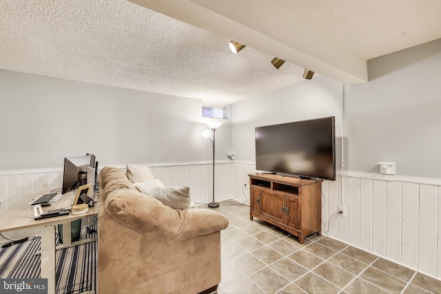 living room featuring wooden walls, light tile patterned flooring, a textured ceiling, and wainscoting