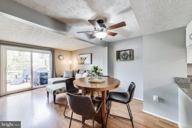 dining area with a ceiling fan, a textured ceiling, baseboards, and light wood-style floors