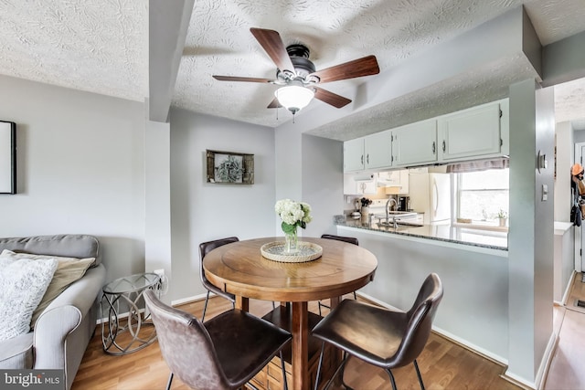 dining area with baseboards, a textured ceiling, ceiling fan, and wood finished floors