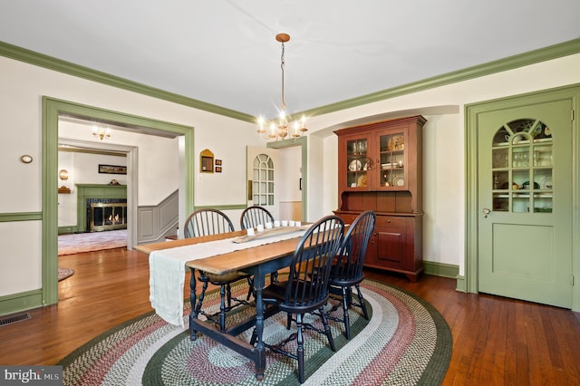 dining space with crown molding, a warm lit fireplace, visible vents, and dark wood-style floors