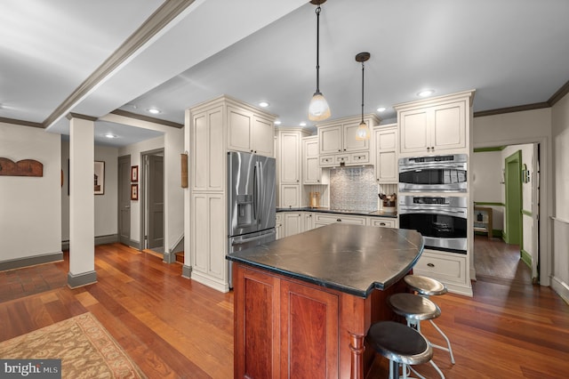kitchen featuring dark countertops, appliances with stainless steel finishes, cream cabinets, tasteful backsplash, and baseboards