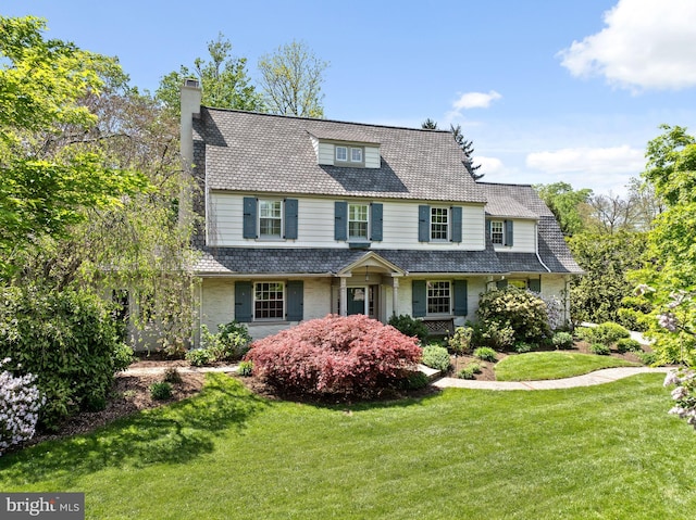 view of front facade with a high end roof, a chimney, brick siding, and a front yard
