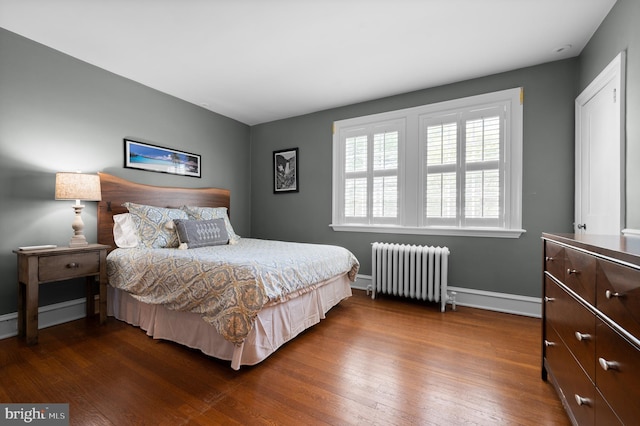 bedroom with dark wood-type flooring, baseboards, and radiator heating unit