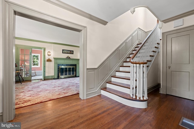 stairway with a fireplace, ornamental molding, and wood-type flooring