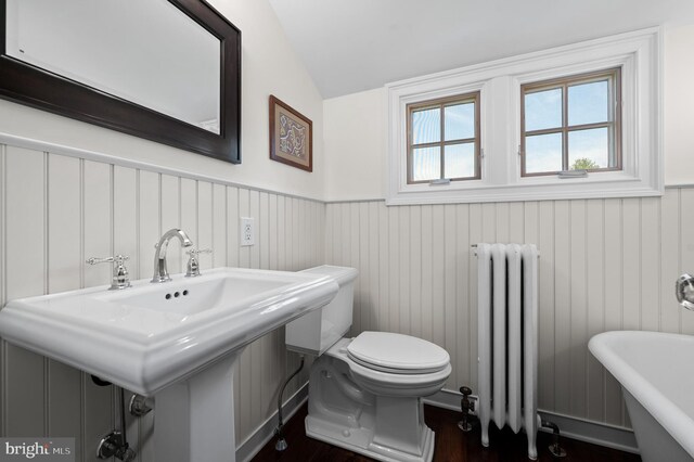 bathroom with toilet, radiator, a wainscoted wall, a freestanding tub, and wood finished floors