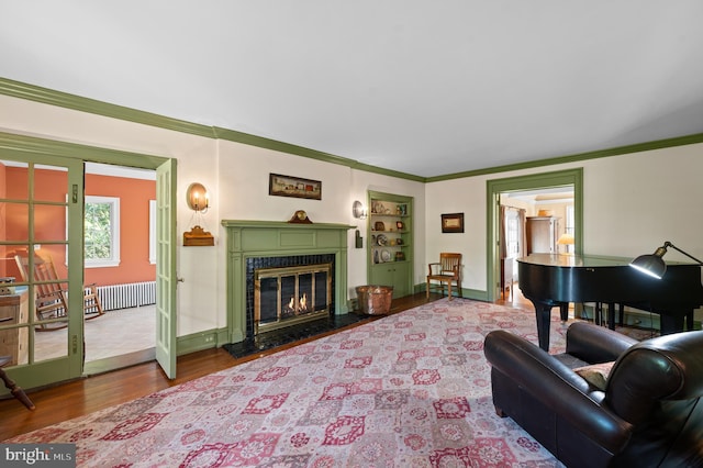 living room with a glass covered fireplace, radiator heating unit, baseboards, wood finished floors, and ornamental molding