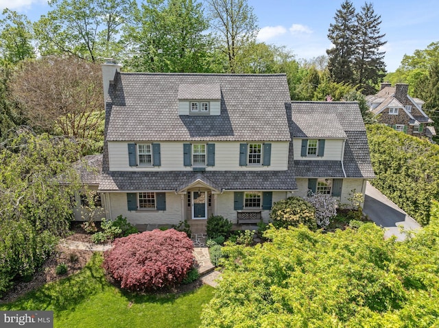 shingle-style home featuring a high end roof, a chimney, and stone siding