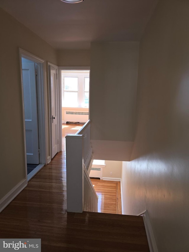 corridor with baseboards, a baseboard radiator, wood finished floors, and an upstairs landing