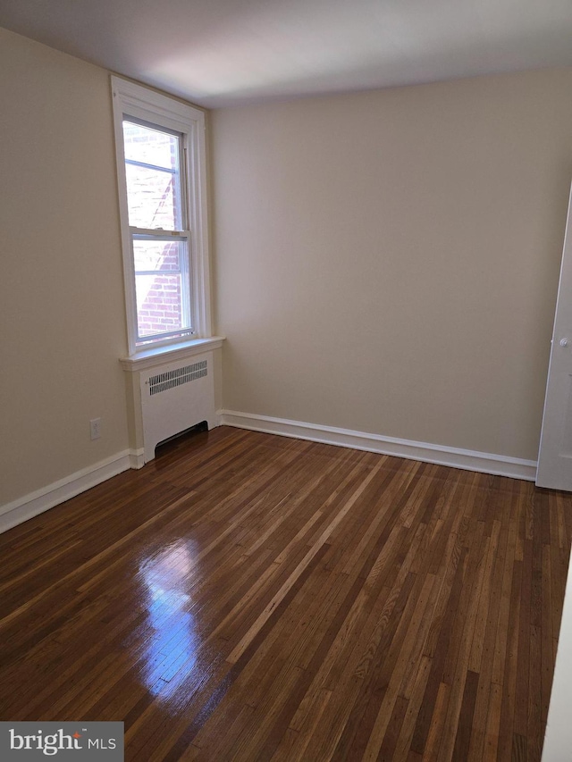empty room with radiator heating unit, baseboards, and dark wood-type flooring