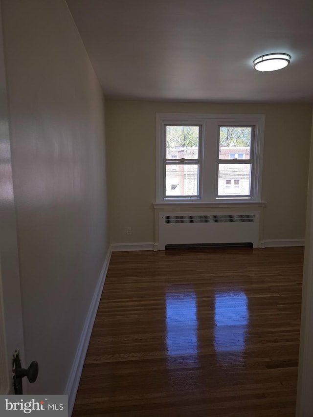 unfurnished room with baseboards, radiator, and wood finished floors