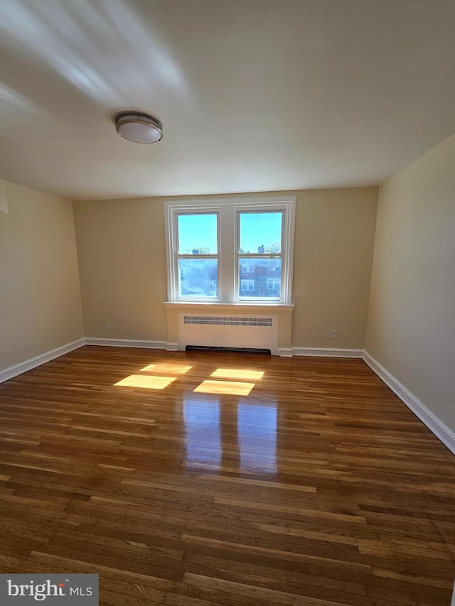 spare room with baseboards, wood finished floors, and radiator