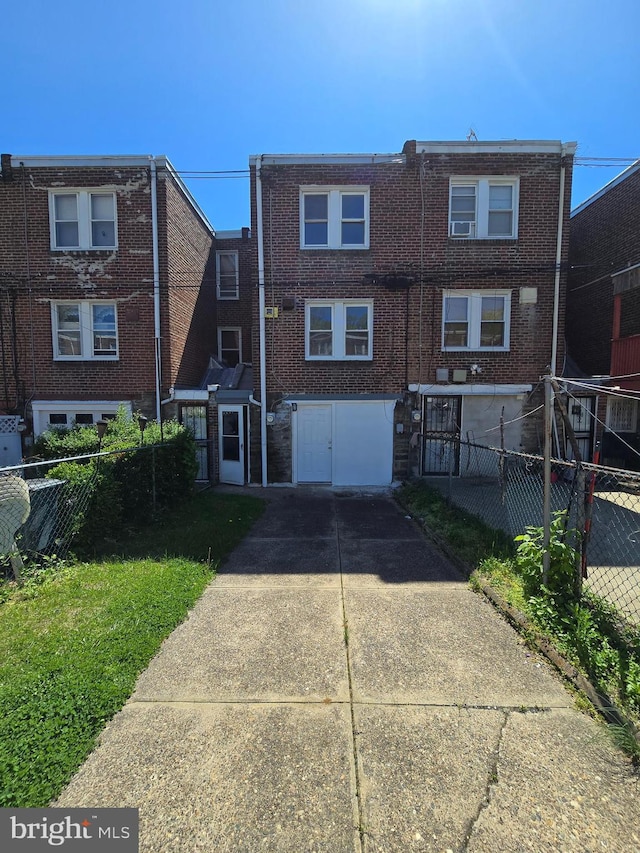 rear view of house featuring brick siding, fence, and driveway