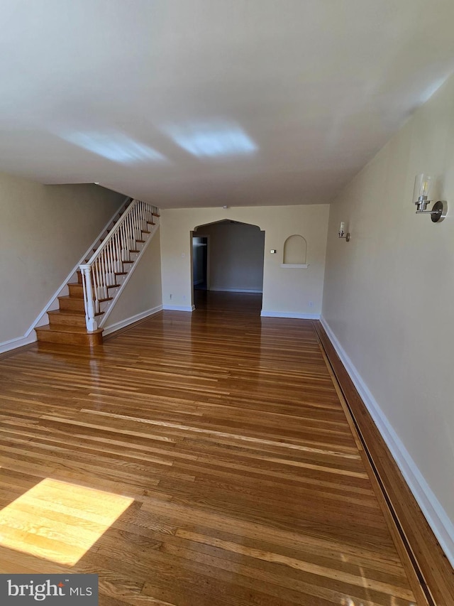 interior space with stairway, arched walkways, baseboards, and wood finished floors