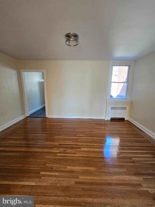 empty room featuring wood finished floors, baseboards, and radiator heating unit