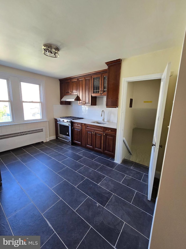 kitchen featuring stainless steel gas range oven, dark tile patterned floors, light countertops, under cabinet range hood, and a sink