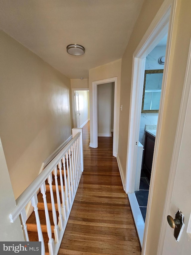 hallway featuring baseboards, wood finished floors, and an upstairs landing
