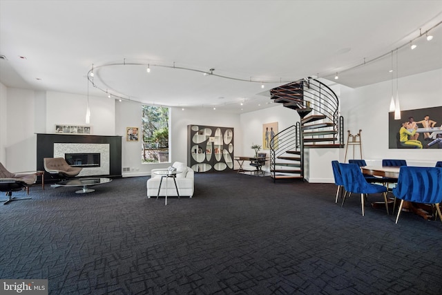 carpeted living room featuring baseboards, rail lighting, a glass covered fireplace, and stairway