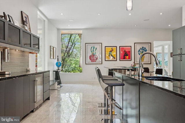 kitchen featuring decorative backsplash, a breakfast bar area, a sink, dark stone counters, and recessed lighting