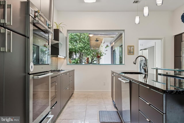 kitchen featuring pendant lighting, a sink, baseboards, dark stone counters, and stainless steel appliances