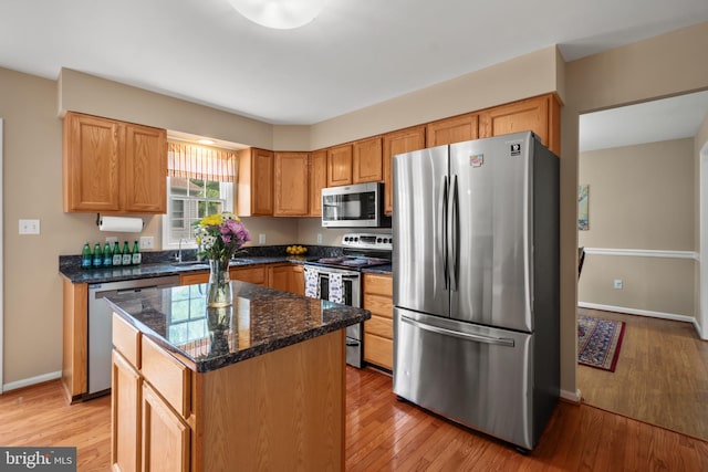 kitchen with appliances with stainless steel finishes, light wood-style flooring, baseboards, a center island, and dark stone counters