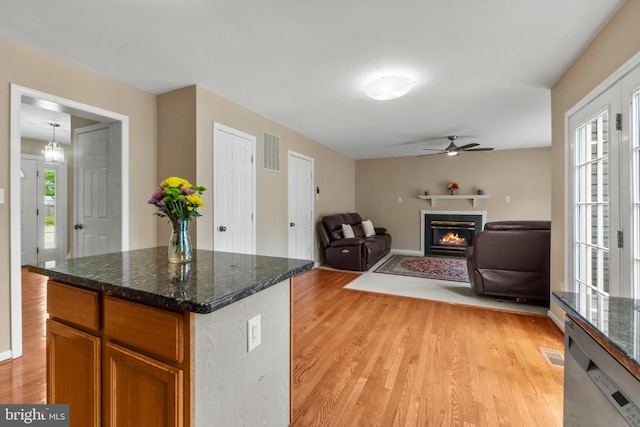 kitchen with light wood-type flooring, a glass covered fireplace, a ceiling fan, brown cabinetry, and open floor plan