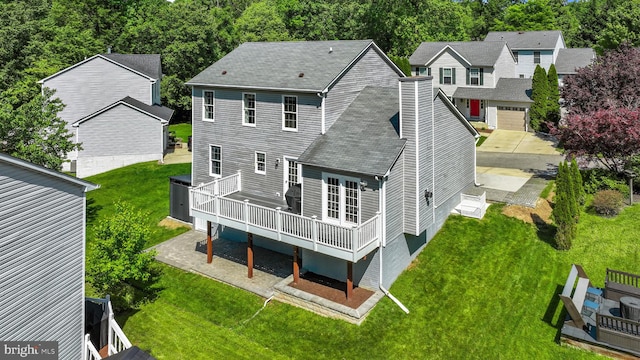 back of property with a deck, a chimney, roof with shingles, and a lawn