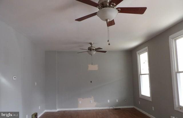empty room with a ceiling fan, baseboards, plenty of natural light, and dark wood-type flooring