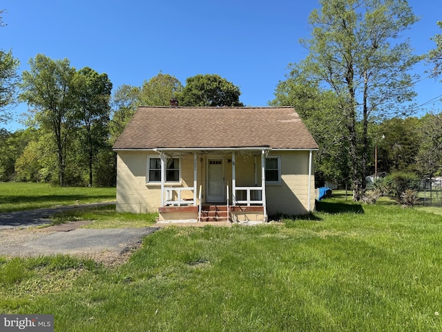 rear view of property with a porch, roof with shingles, a yard, and concrete block siding