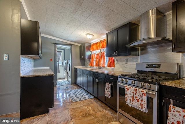 kitchen featuring wall chimney range hood, washing machine and clothes dryer, tasteful backsplash, gas stove, and a sink