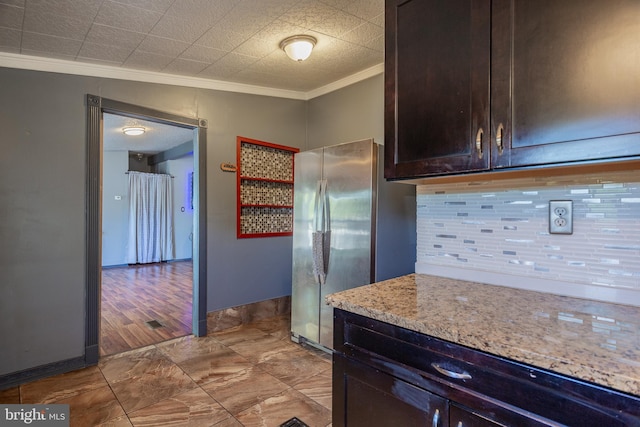kitchen featuring crown molding, light stone countertops, dark brown cabinetry, freestanding refrigerator, and decorative backsplash