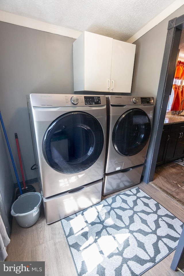 laundry room featuring a textured ceiling, independent washer and dryer, cabinet space, and wood finished floors