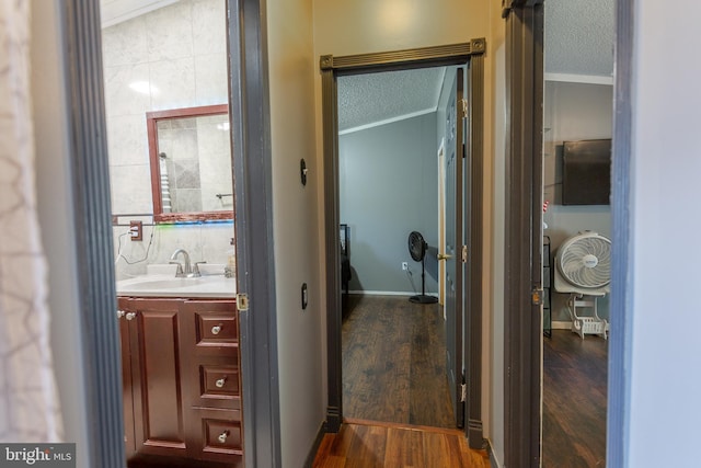 hallway featuring a sink, a textured ceiling, dark wood finished floors, and ornamental molding