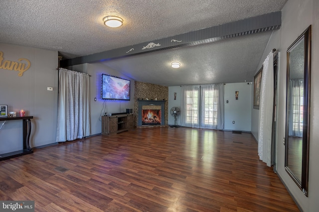 unfurnished living room featuring a textured ceiling, a large fireplace, baseboards, vaulted ceiling with beams, and wood finished floors