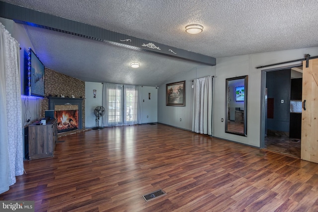 unfurnished living room with wood finished floors, lofted ceiling with beams, a barn door, and visible vents