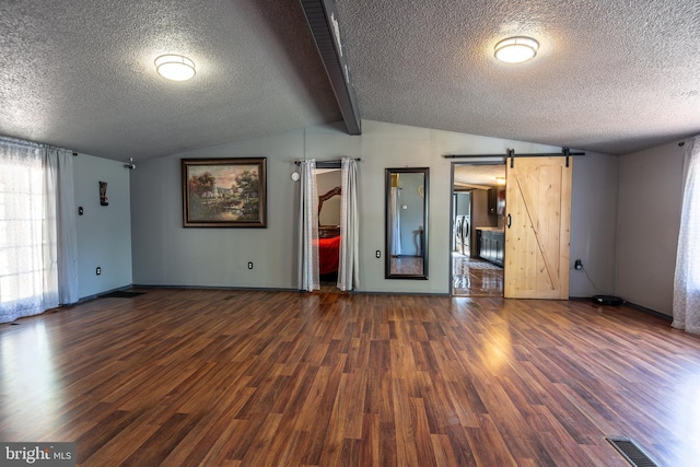unfurnished living room featuring a barn door, a textured ceiling, wood finished floors, and visible vents