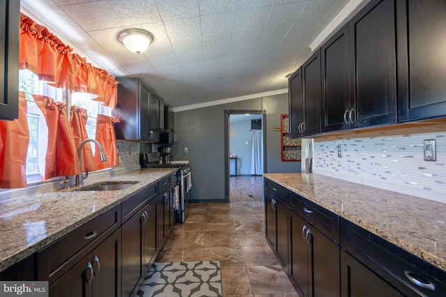 kitchen with stainless steel range with gas stovetop, tasteful backsplash, light stone countertops, a sink, and ornamental molding