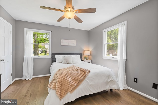 bedroom with baseboards, multiple windows, and wood finished floors