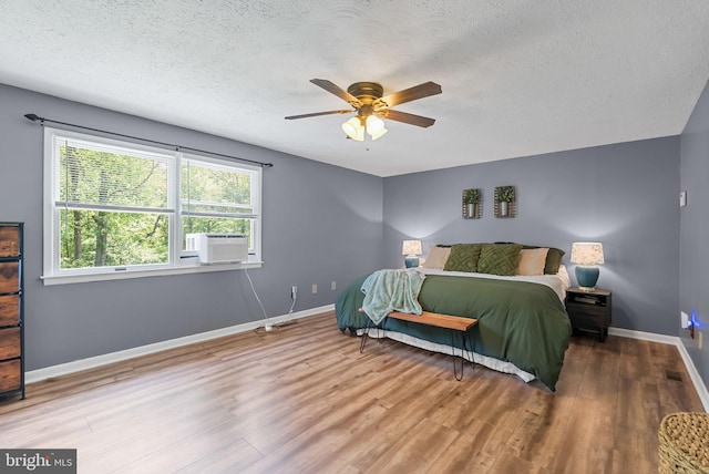 bedroom with ceiling fan, cooling unit, a textured ceiling, baseboards, and wood finished floors