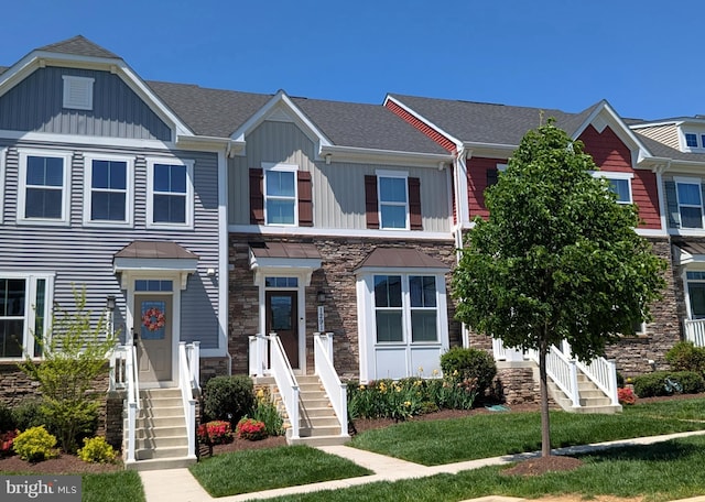 townhome / multi-family property featuring roof with shingles, board and batten siding, and stone siding