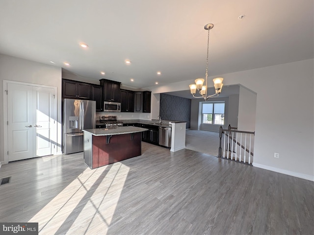 kitchen featuring appliances with stainless steel finishes, a center island, light wood finished floors, open floor plan, and an inviting chandelier